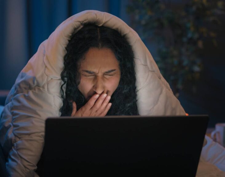 Tired Hispanic girl exhausted sleepy woman fatigued Indian Arabian female at night evening home couch sofa under blanket cover duvet working with laptop watching movie computer addict yawn need sleep. High quality 4k footage